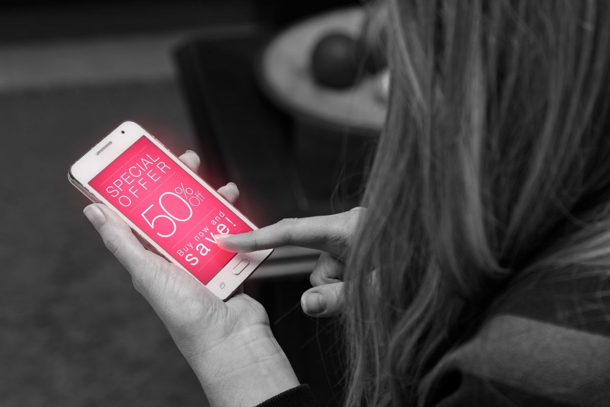 Woman holding a smartphone with a 50% Off discount advertising on the screen. Marketing, ecommerce, cell phone publicity. Black and white version.